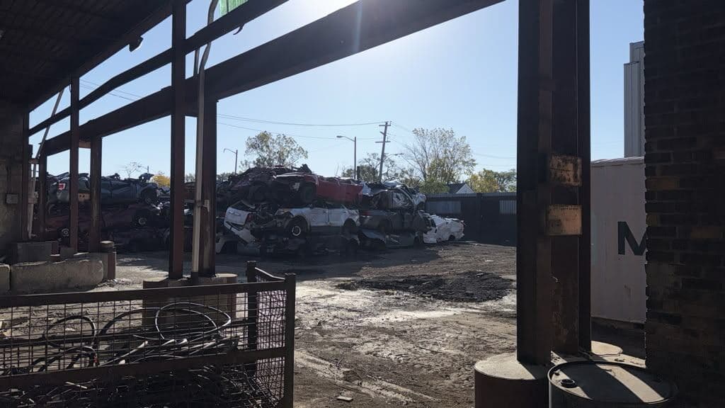 Vehicles stacked for processing under a steel canopy at the recycling yard